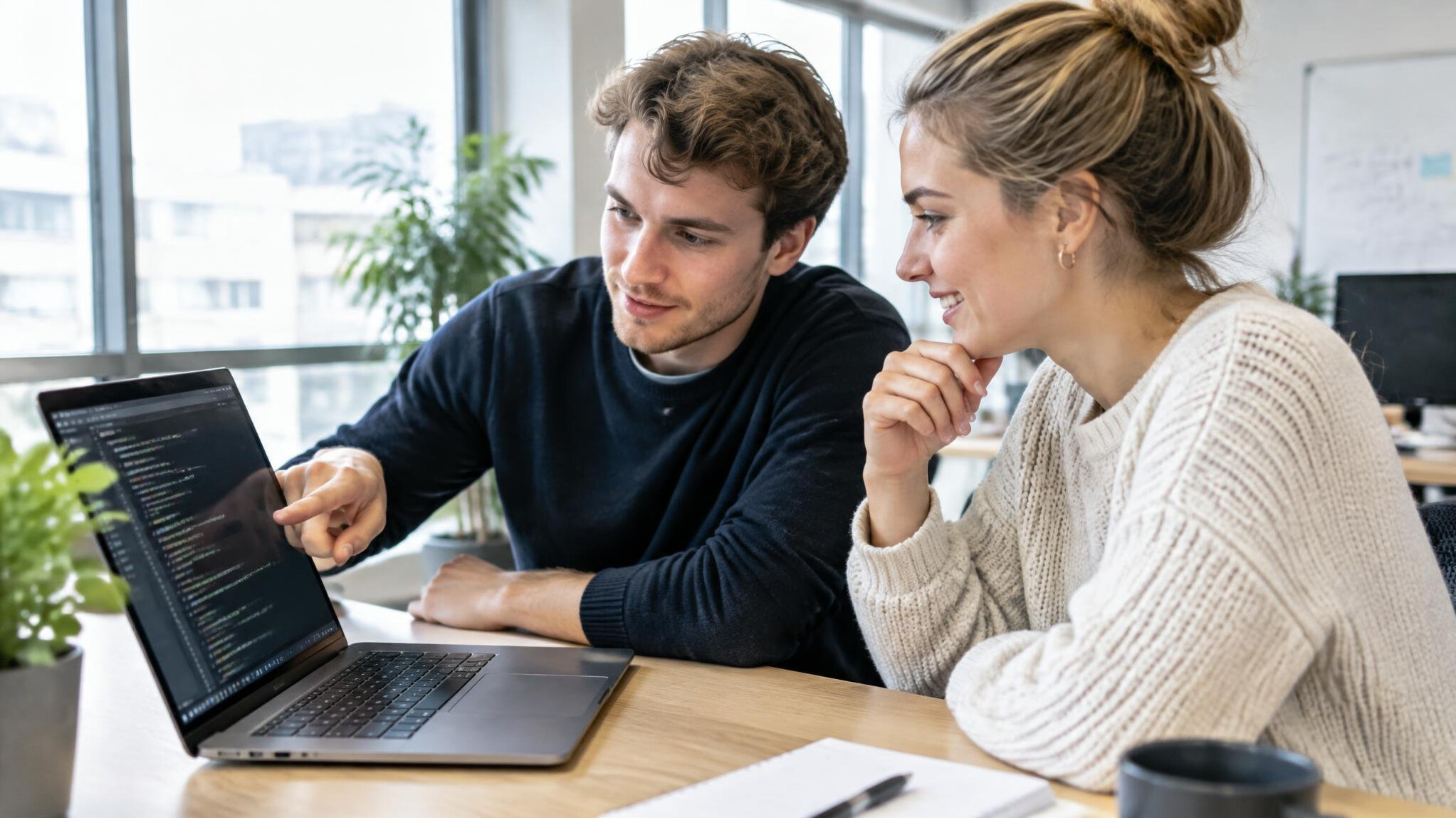 Two colleagues reviewing code together on a laptop